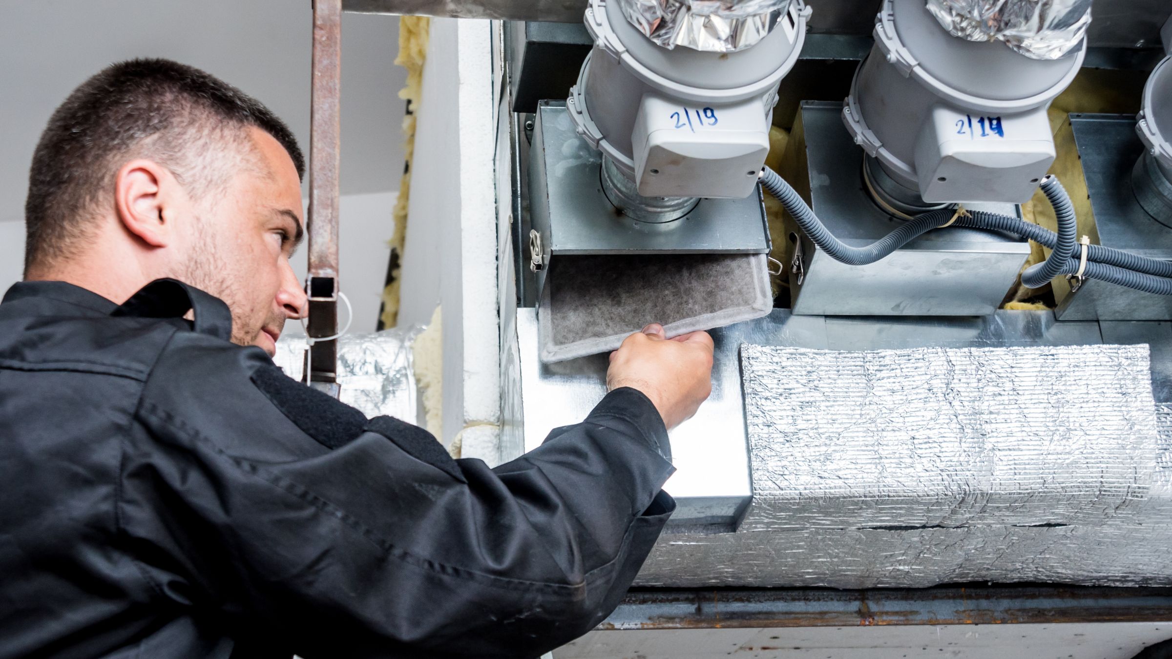 Wentylacja na Śląsku AirClean Serwisant kontroluje filtr w instalacji wentylacyjnej z kanałami i urządzeniami zamontowanymi w zabudowie technicznej. Zdjęcie ilustruje montaż i obsługę wentylacji na Śląsku. Więcej informacji o usłudze znajdziesz na stronie AirClean.